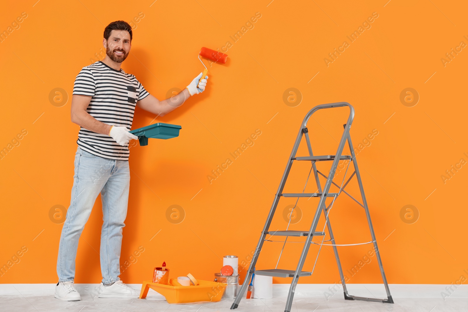 Photo of Designer painting orange wall with roller indoors