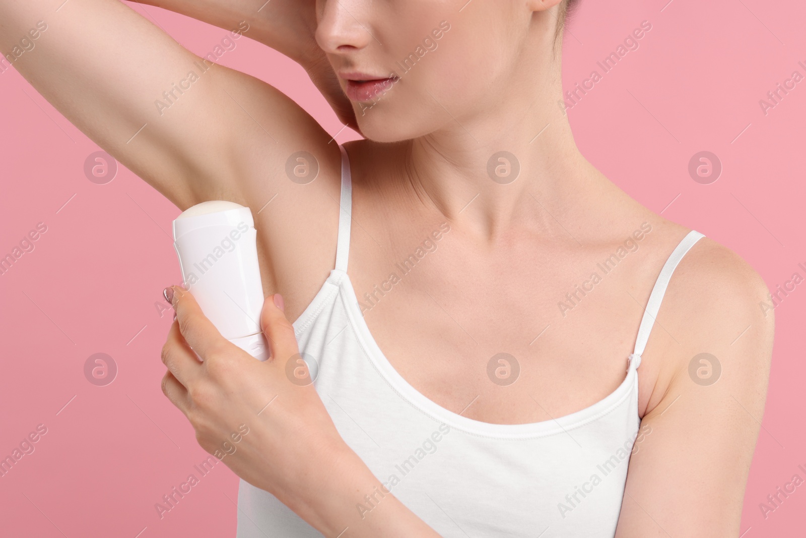 Photo of Woman applying deodorant on pink background, closeup