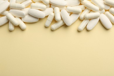 Vitamin pills on pale yellow background, flat lay. Space for text