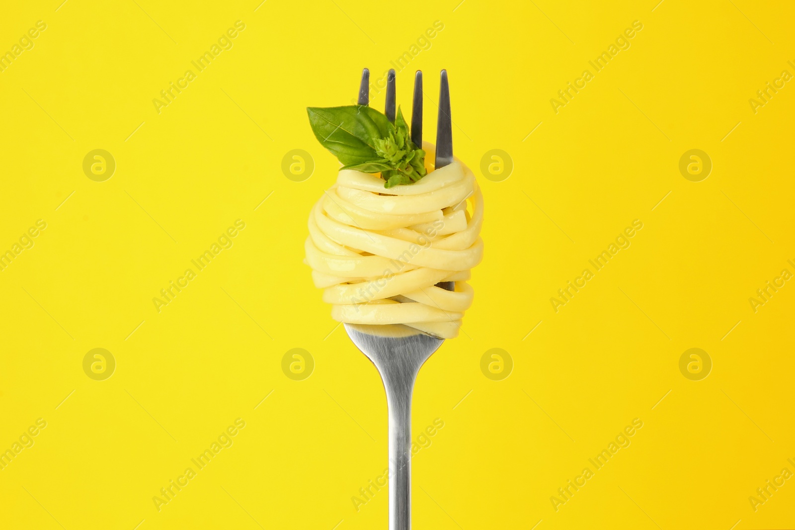 Photo of Fork with tasty pasta and basil on yellow background