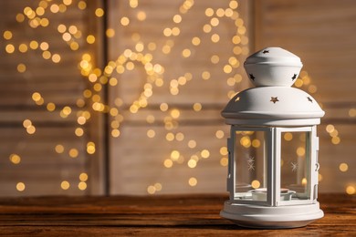 Photo of Beautiful white decorative lantern on wooden table against blurred lights, space for text