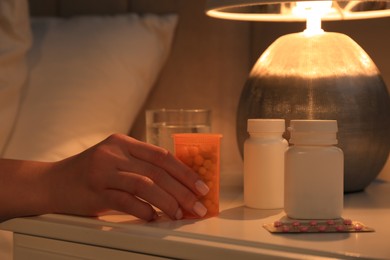 Photo of Woman taking pills from nightstand indoors, closeup. Insomnia treatment
