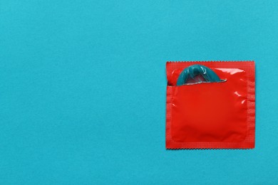 Photo of Condom in torn package on light blue background, top view with space for text. Safe sex