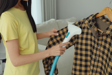 Photo of Woman steaming shirt on hanger at home, closeup