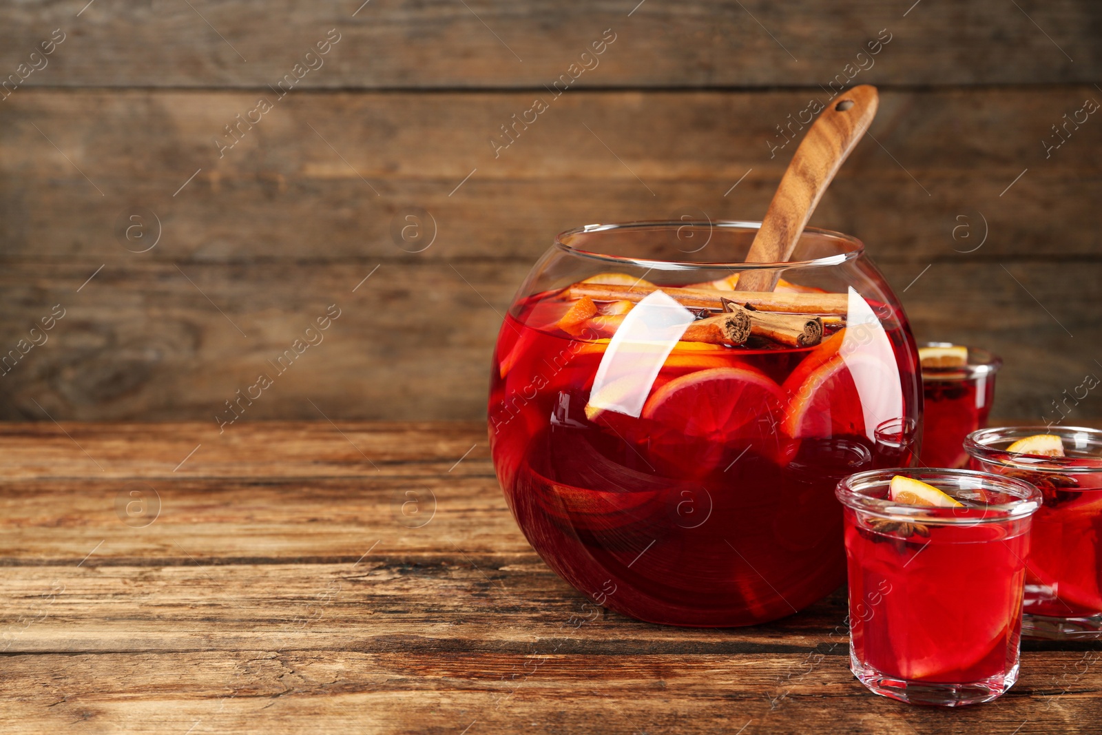 Photo of Glasses and bowl of delicious aromatic punch drink on wooden table. Space for text