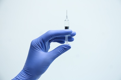 Doctor holding syringe with COVID-19 vaccine on light background, closeup