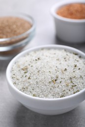 Photo of Different kinds of salt in bowls on grey table, closeup