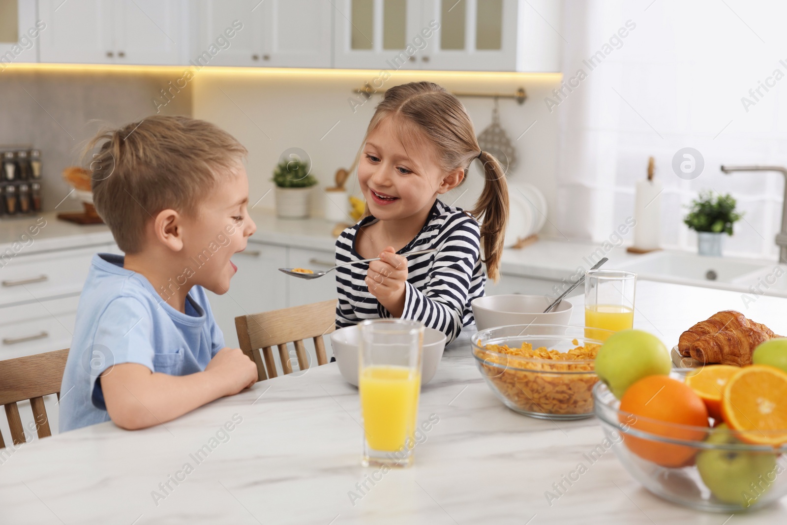 Photo of Little children having breakfast at table in kitchen