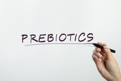 Woman writing word PREBIOTICS on glass against white background, closeup