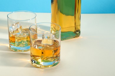 Photo of Whiskey with ice cubes in glasses and bottle on white table, space for text