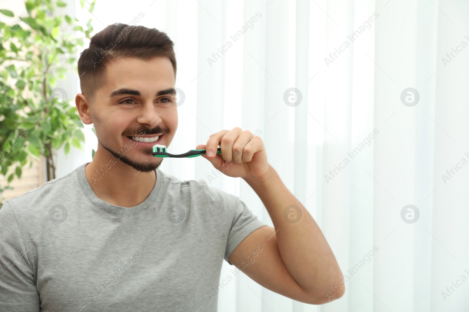 Photo of Young man brushing teeth in bathroom at home. Space for text