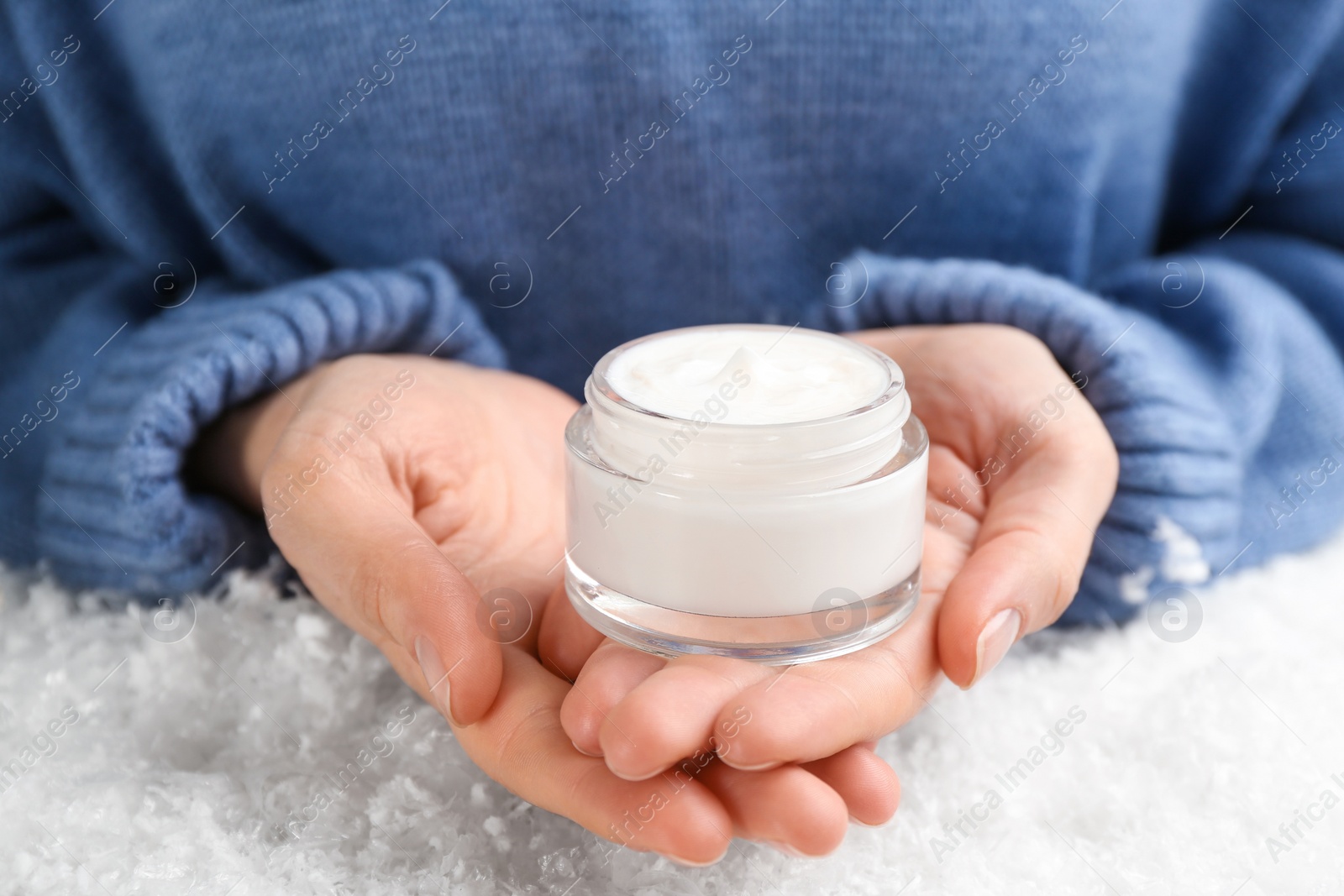 Photo of Woman holding jar of cream above decorative snow, closeup. Cosmetic product for winter