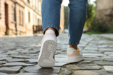 Woman in stylish sneakers walking on city street, closeup