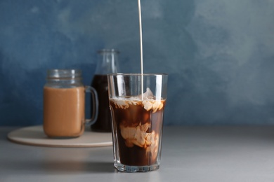 Photo of Pouring milk into glass with cold brew coffee on table