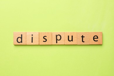 Word Dispute made with wooden cubes on light green background, top view