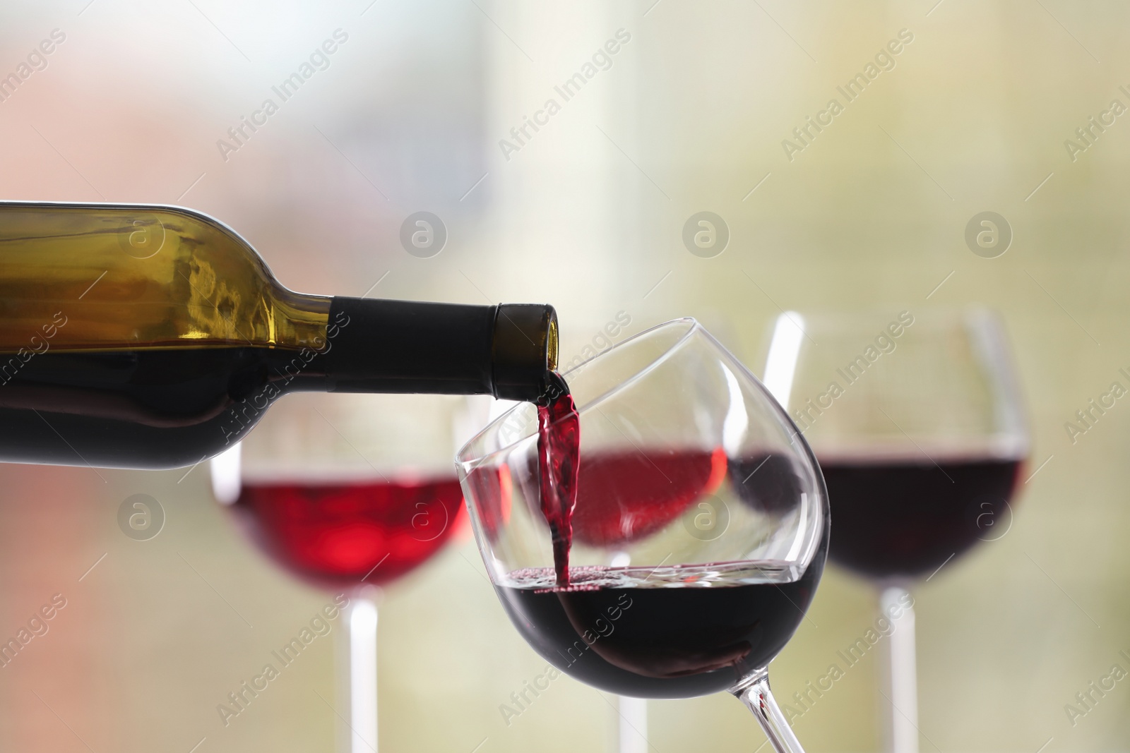 Photo of Pouring red wine from bottle into glass on blurred background, closeup