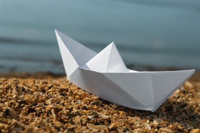 Photo of White paper boat near river on sunny day, closeup