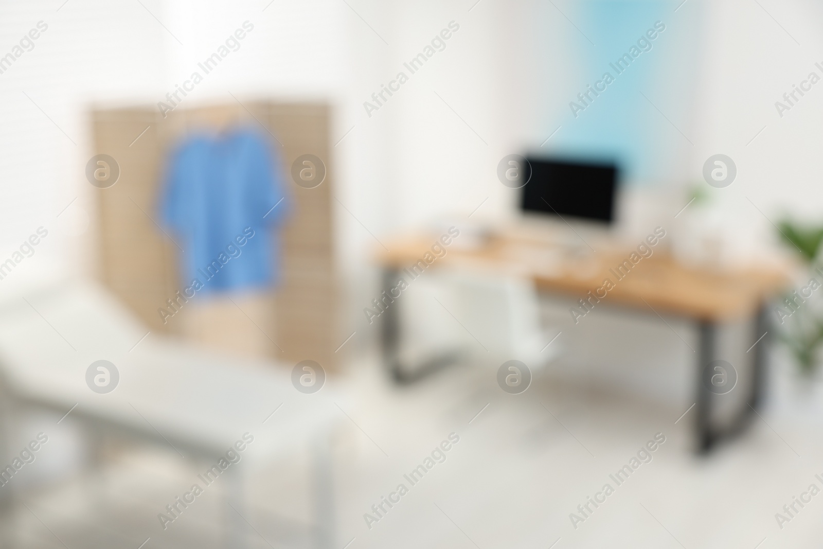 Photo of Blurred view of modern medical office with doctor's workplace and examination table in clinic