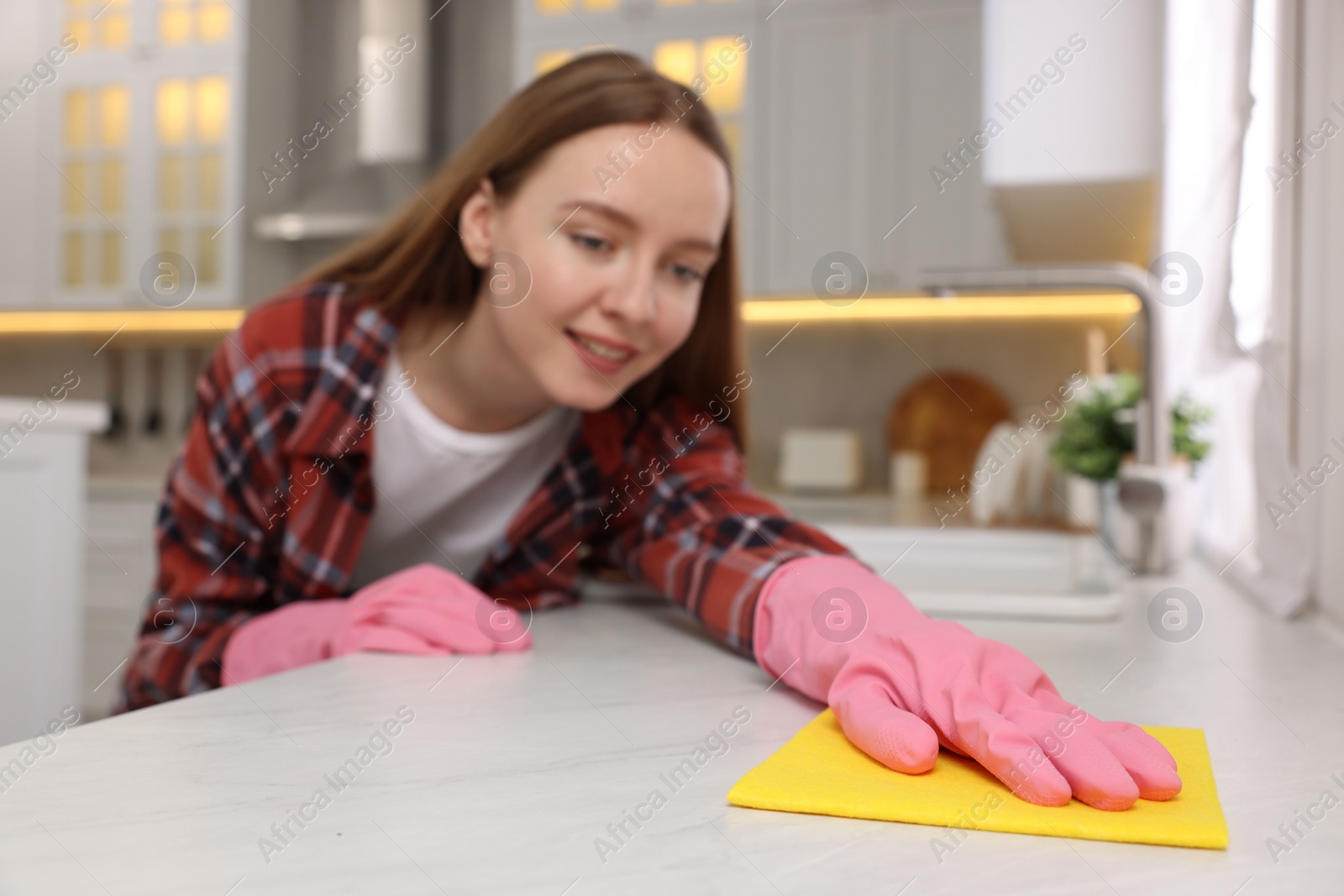 Photo of Woman cleaning white marble table with microfiber cloth in kitchen, selective focus