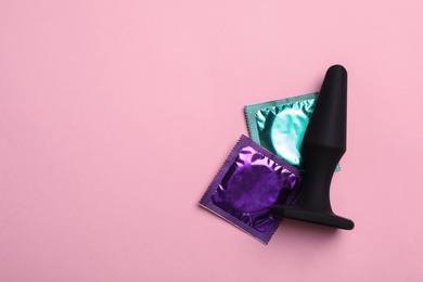 Photo of Anal plug and condoms on pink background, top view with space for text. Sex game