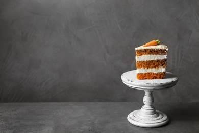 Stand with piece of carrot cake on grey table, space for text