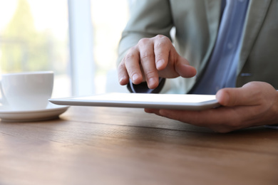 Photo of Businessman working with modern tablet at wooden table in office, closeup