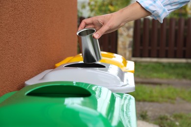 Woman throwing tin can into recycling bin outdoors, closeup