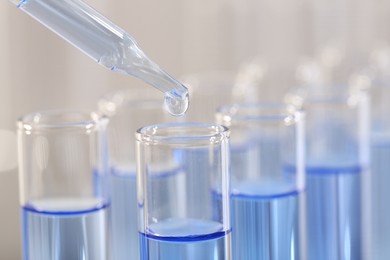 Photo of Laboratory analysis. Dripping light blue liquid from pipette into glass test tube on blurred background, closeup