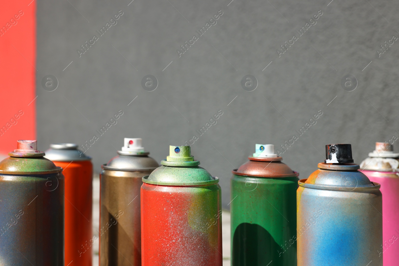 Photo of Cans of different spray paints near wall outdoors, closeup