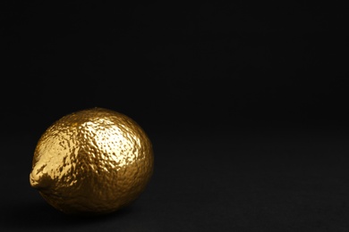 Photo of Lemon painted gold on black background. Space for text