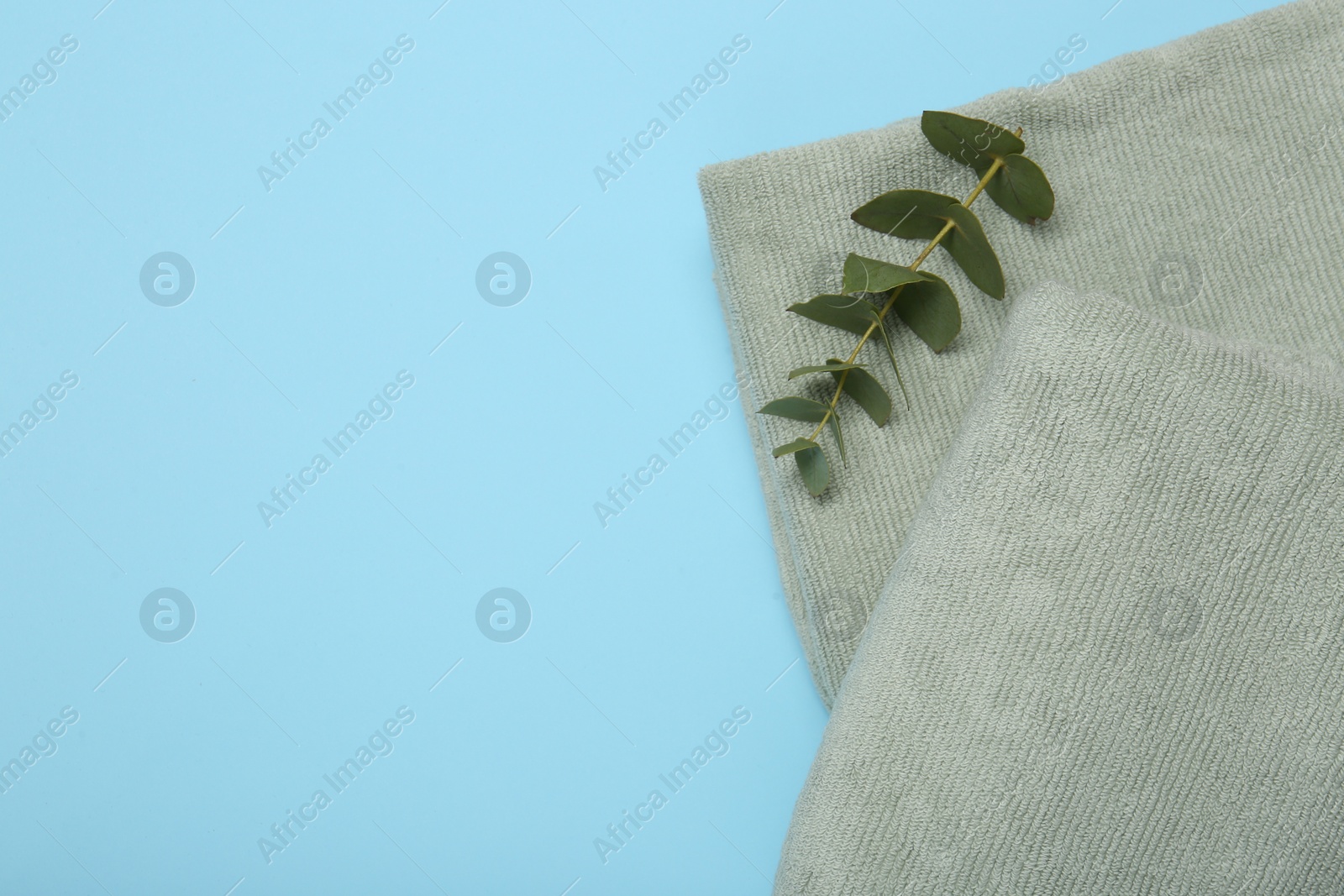 Photo of Terry towels and eucalyptus branch on light blue background, top view. Space for text