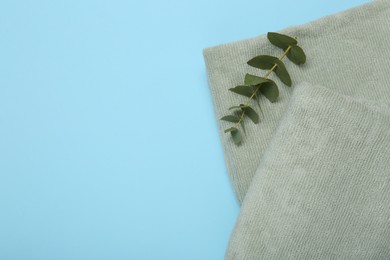 Photo of Terry towels and eucalyptus branch on light blue background, top view. Space for text
