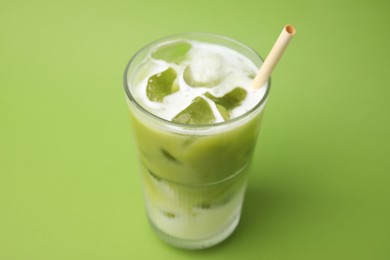 Photo of Glass of tasty iced matcha latte on light green background, closeup