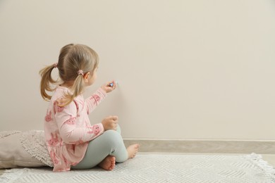 Little girl drawing on beige wall indoors, space for text. Child`s art