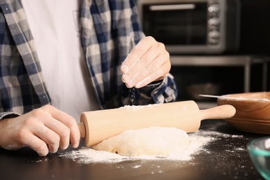 Man sprinkling flour while rolling dough on table in kitchen