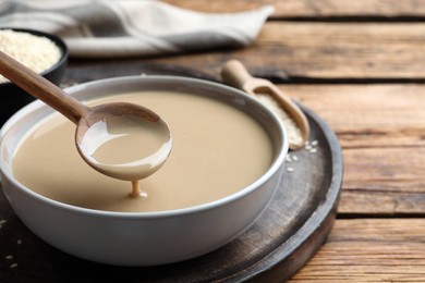 Photo of Spoon with tasty sesame paste over bowl on wooden table, closeup