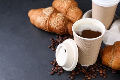 Photo of Coffee to go. Paper cup with tasty drink, croissants and beans on black table, space for text
