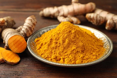 Photo of Plate with aromatic turmeric powder and cut roots on wooden table, closeup