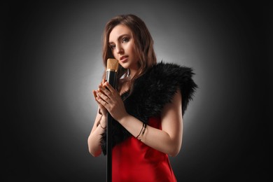 Beautiful young woman with microphone singing on black background