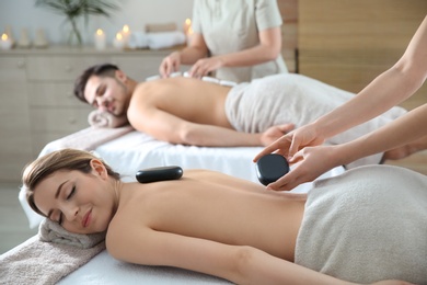 Photo of Romantic young couple enjoying hot stone massage in spa salon