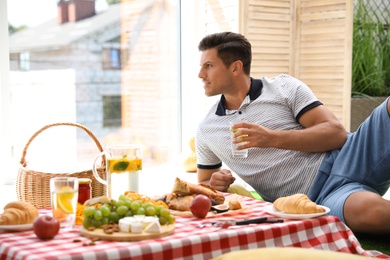 Photo of Man with tasty food and drink imitating picnic at home