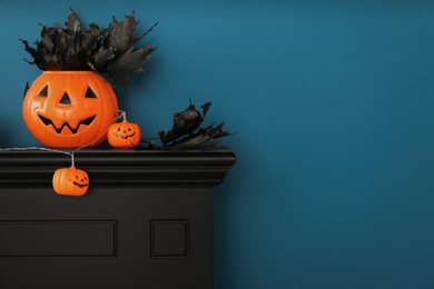 Photo of Jack-o'-lantern lights and black maple leaves on wooden fireplace near blue wall, space for text