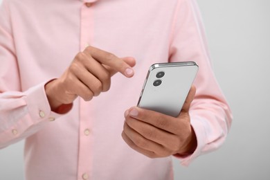Photo of Young man sending message via smartphone on light grey background, closeup