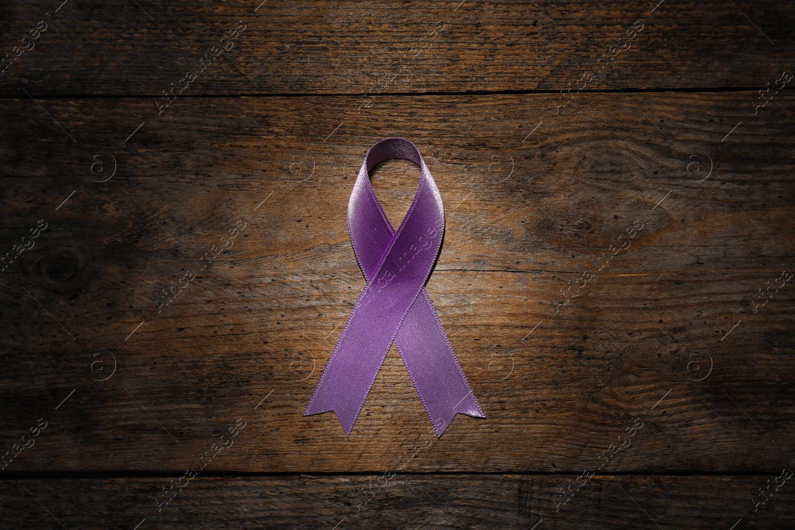 Photo of Purple ribbon on brown wooden background, top view. Domestic violence awareness