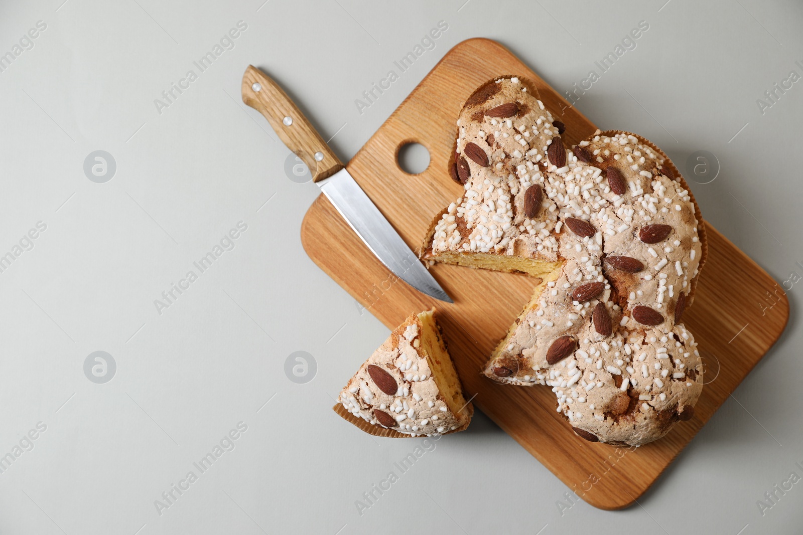 Photo of Delicious Italian Easter dove cake (traditional Colomba di Pasqua) and knife on light table, top view. Space for text
