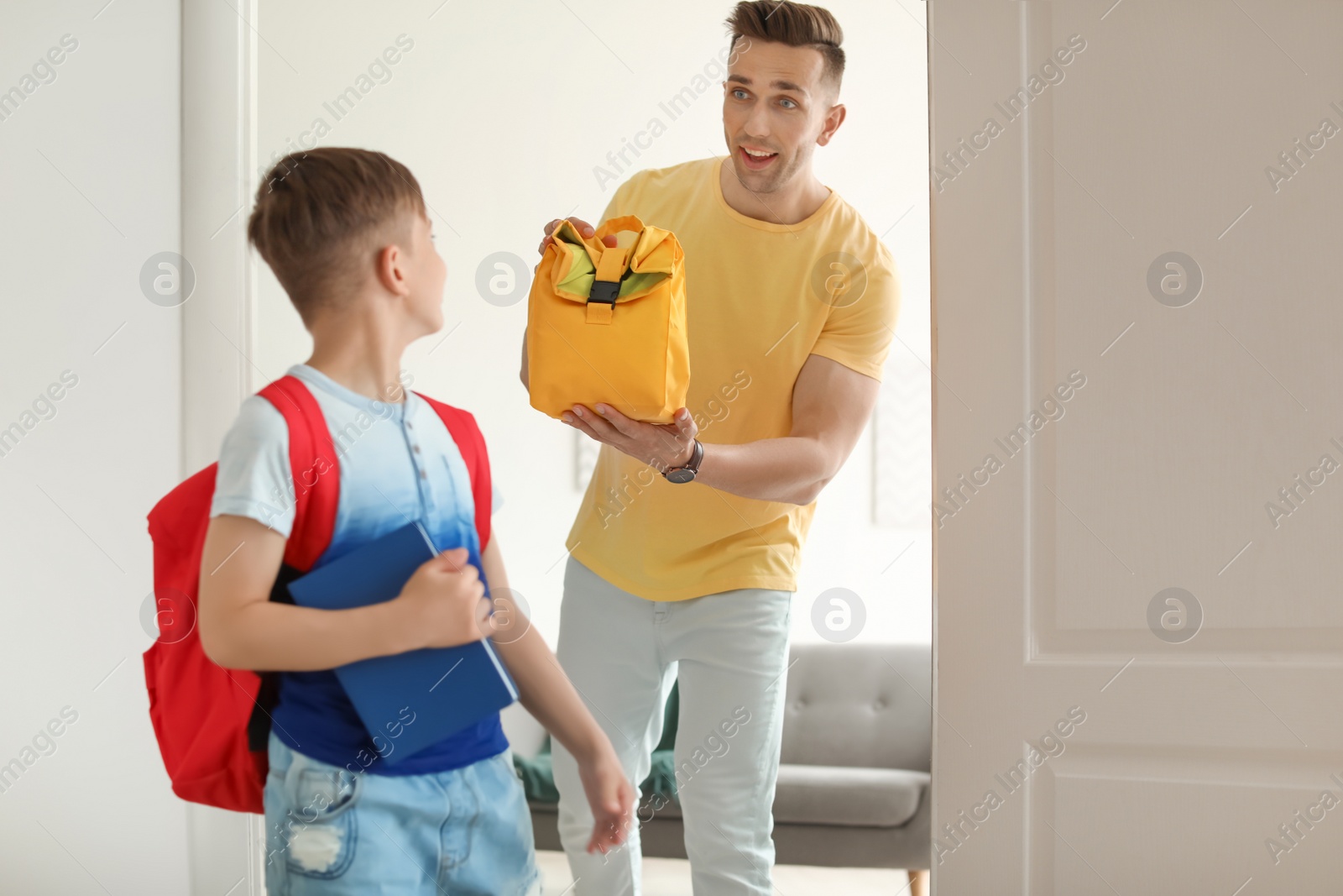 Photo of Young man reminding his little child to take lunch bag as he leaving for school