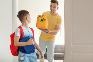 Photo of Young man reminding his little child to take lunch bag as he leaving for school