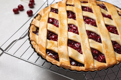 Photo of Delicious fresh cherry pie and cooling tray on light grey table, closeup