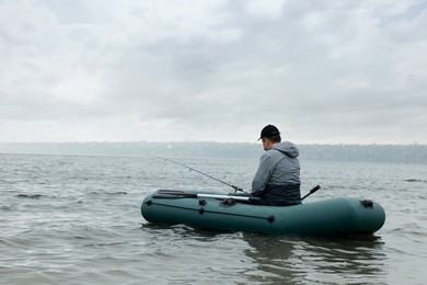 Man fishing with rod from inflatable rubber boat on river