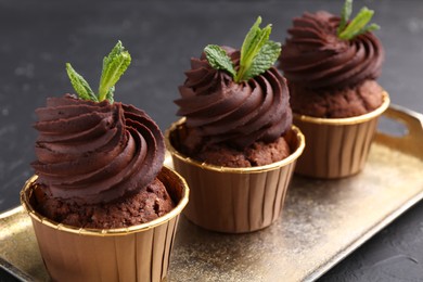 Photo of Delicious chocolate cupcakes with mint on black textured table, closeup